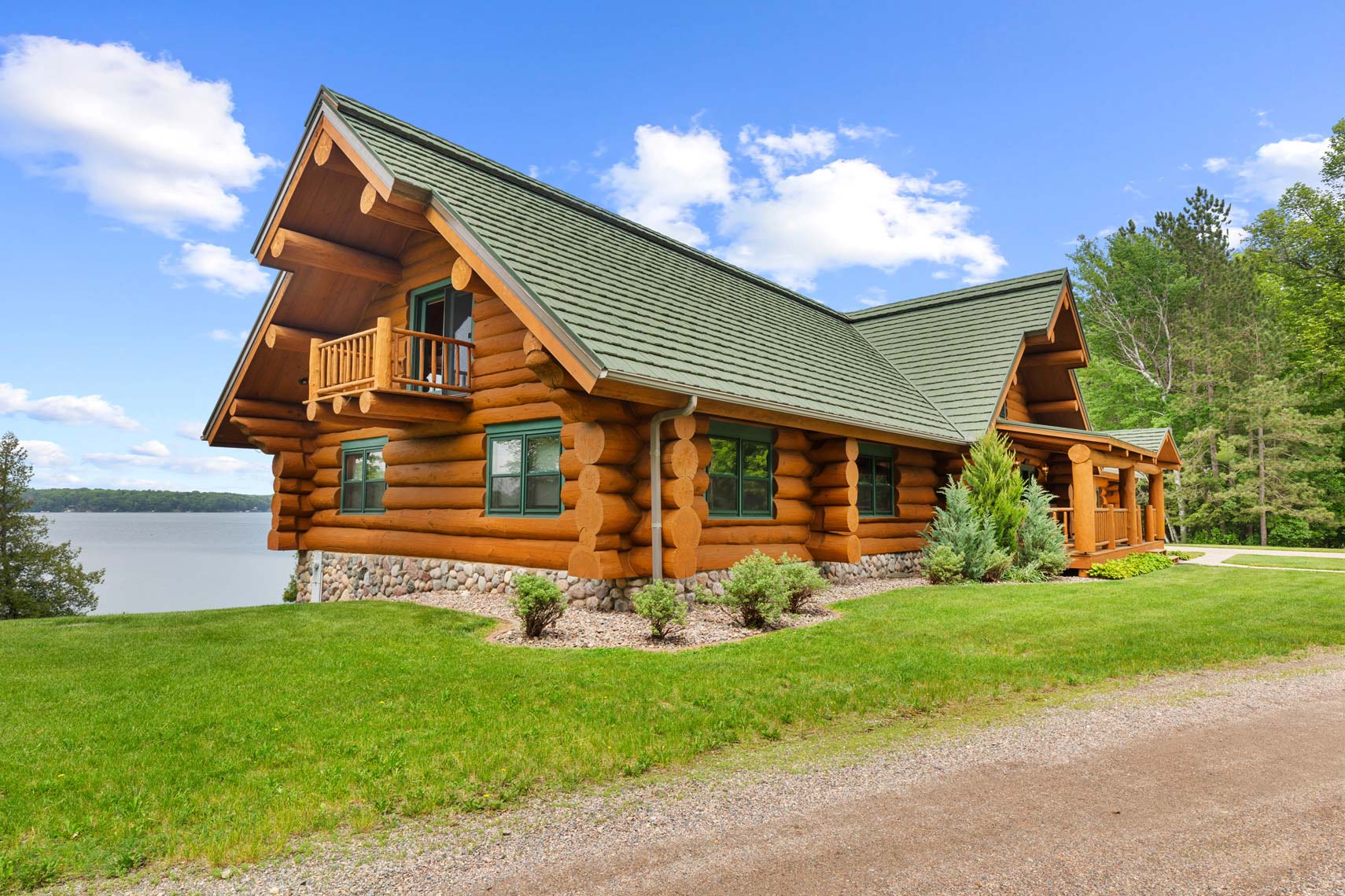 A stunning residential log cabin with a green roof located by the lakeside, surrounded by lush greenery and trees under a partly cloudy sky, ideal for vacation rental property listings.