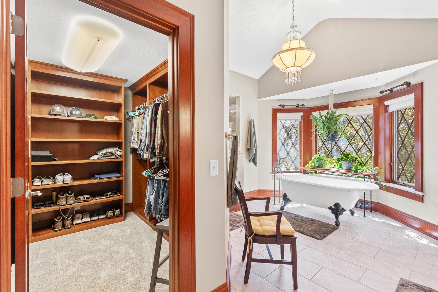 Residential property interior showcasing a luxurious walk-in closet and an adjacent bathroom with a freestanding bathtub, designer chair, large windows for natural light, and elegant pendant lighting.
