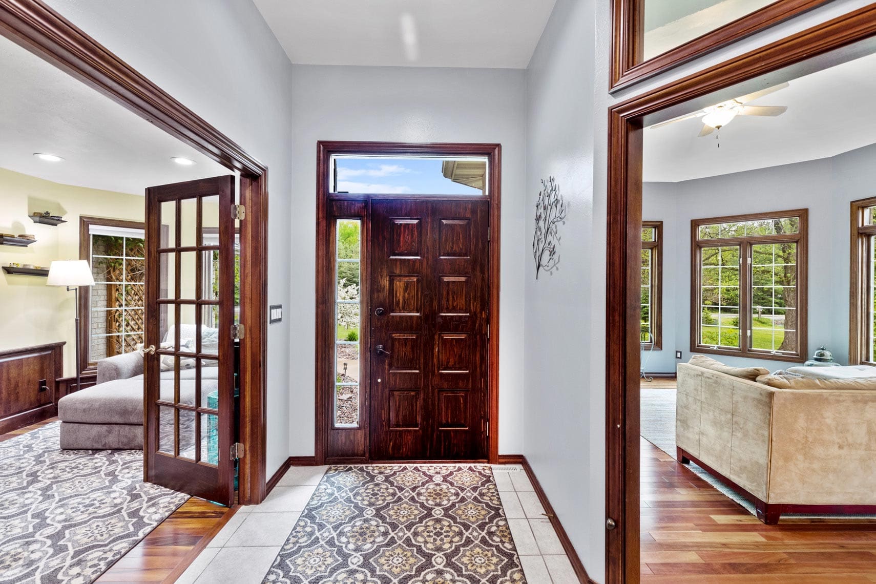 Residential property foyer featuring a dark wood door, tile and wood flooring, with adjacent living areas adorned with sofas and large windows.