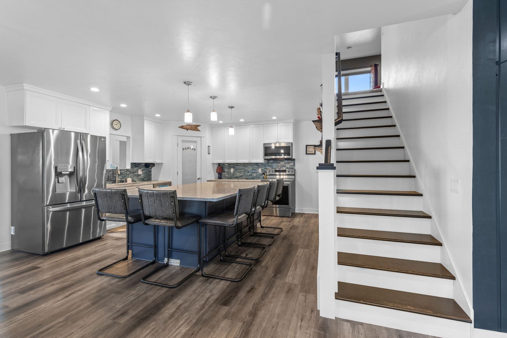 Contemporary residential kitchen featuring a spacious island with barstools, high-end stainless steel appliances, and an elegant staircase for real estate listing.