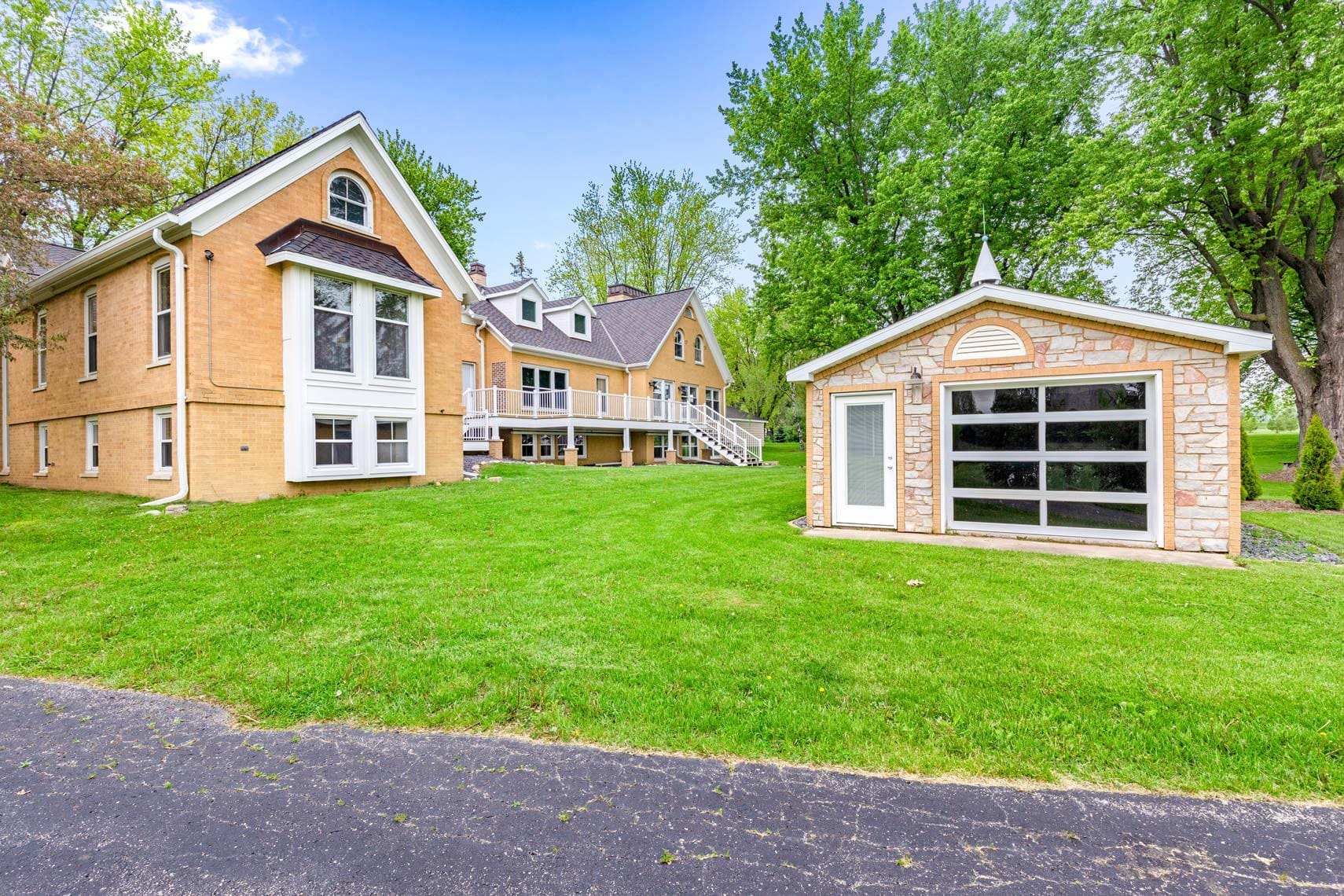 Stunning residential property showcasing a large brick and stone house with multiple gables, an outbuilding, expansive grassy lawn, and encircled by lush trees.