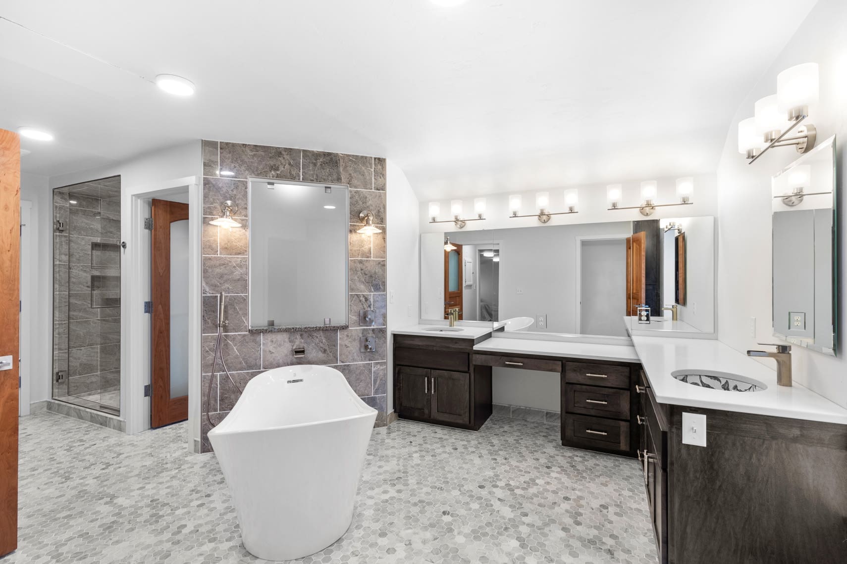 Luxury residential bathroom featuring a freestanding tub, dual sinks, large mirrors, stone-tiled shower, and modern wall-mounted lighting fixtures.