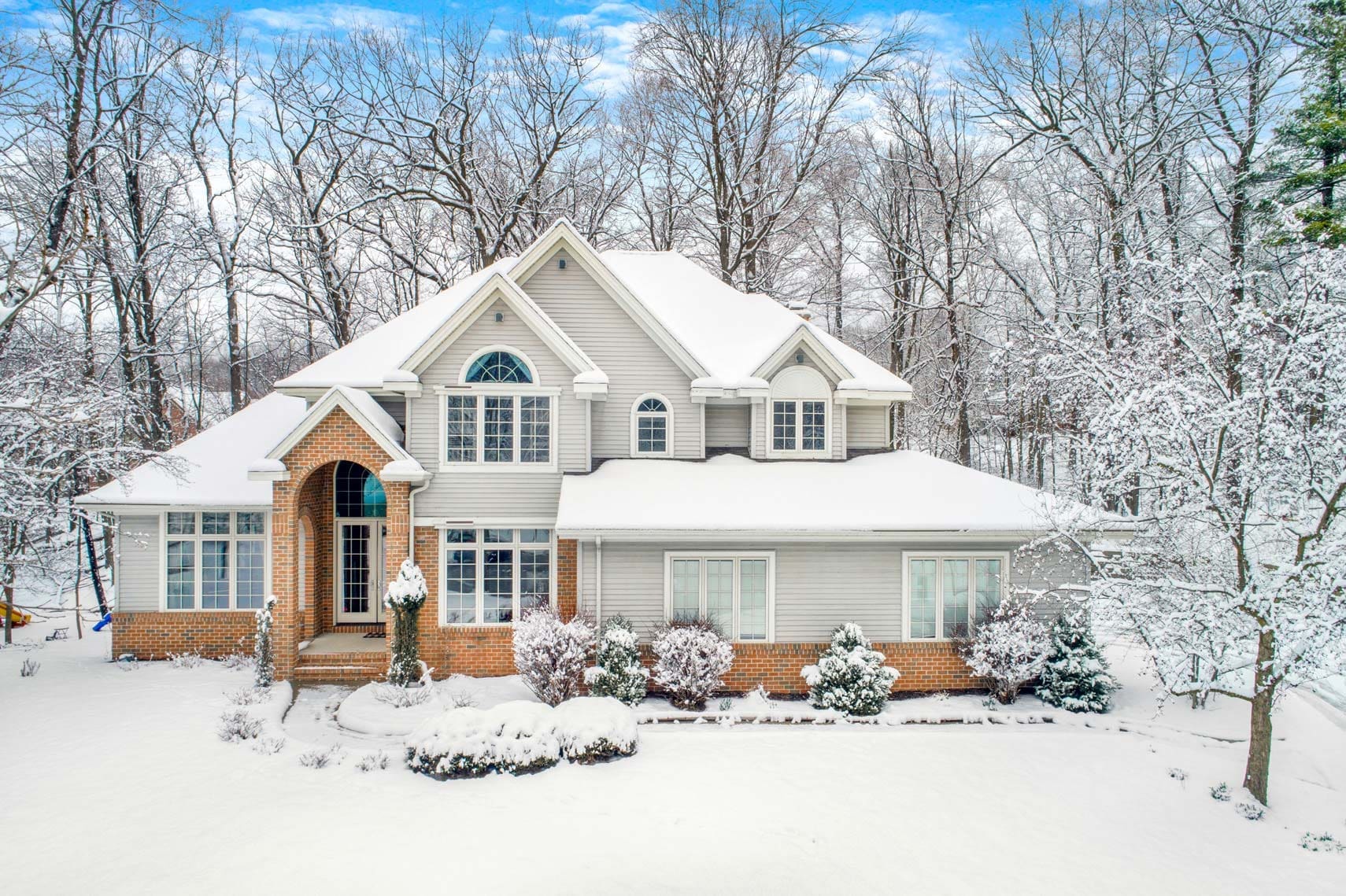 Stunning two-story residential property with a snow-covered roof and spacious yard, surrounded by bare trees on a clear winter day, ideal for the real estate market.