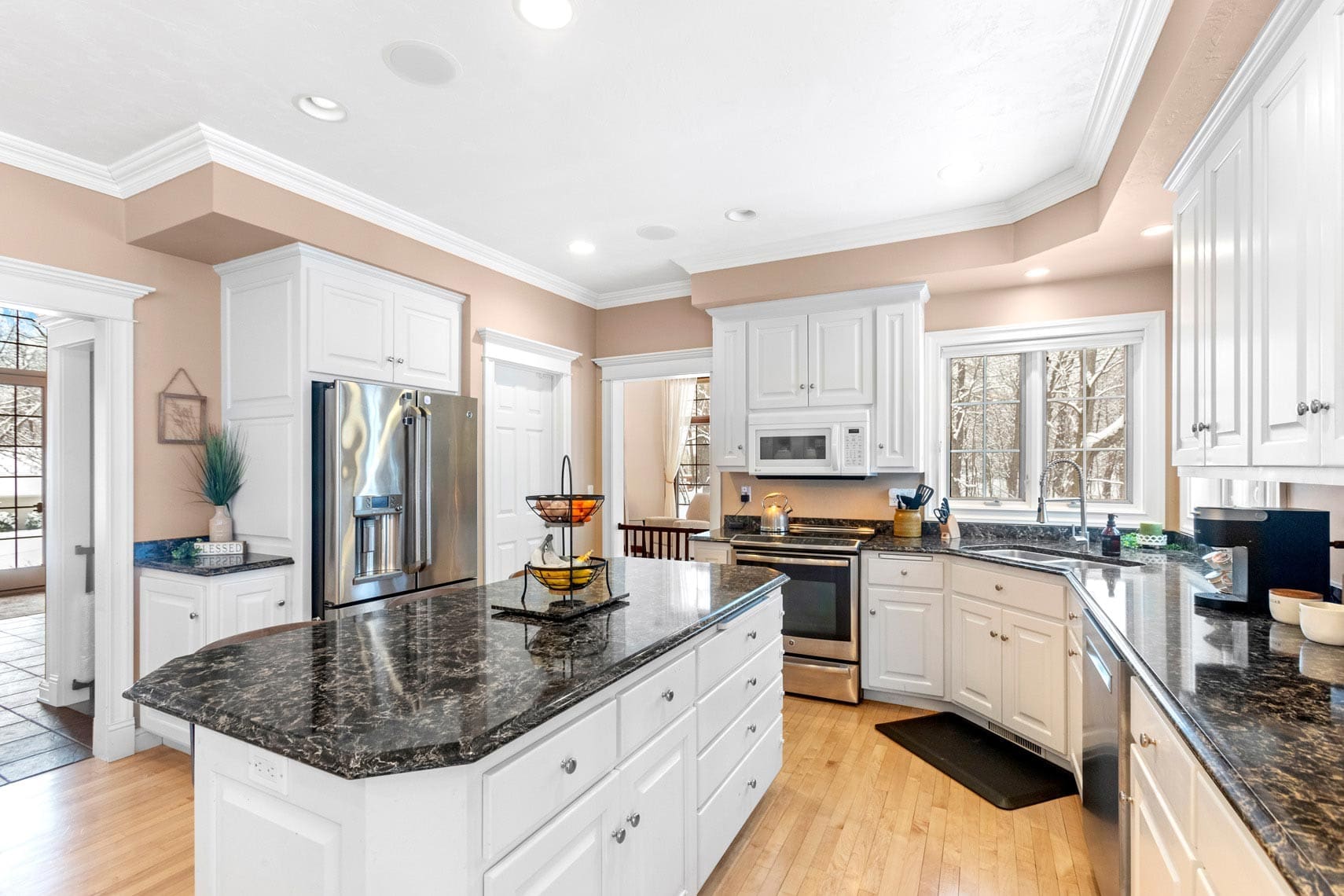 Expansive residential kitchen featuring white cabinetry, black granite countertops, hardwood floors, and stainless steel appliances with a central island. Large windows allow abundant natural light into this prime real estate amenity.
