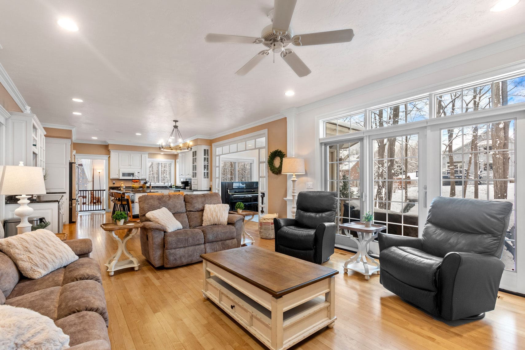 Expansive residential living room featuring plush sofas, armchairs, and a central coffee table with abundant natural light streaming through large windows. Open-concept kitchen visible in the background, ideal for real estate showcasing.
