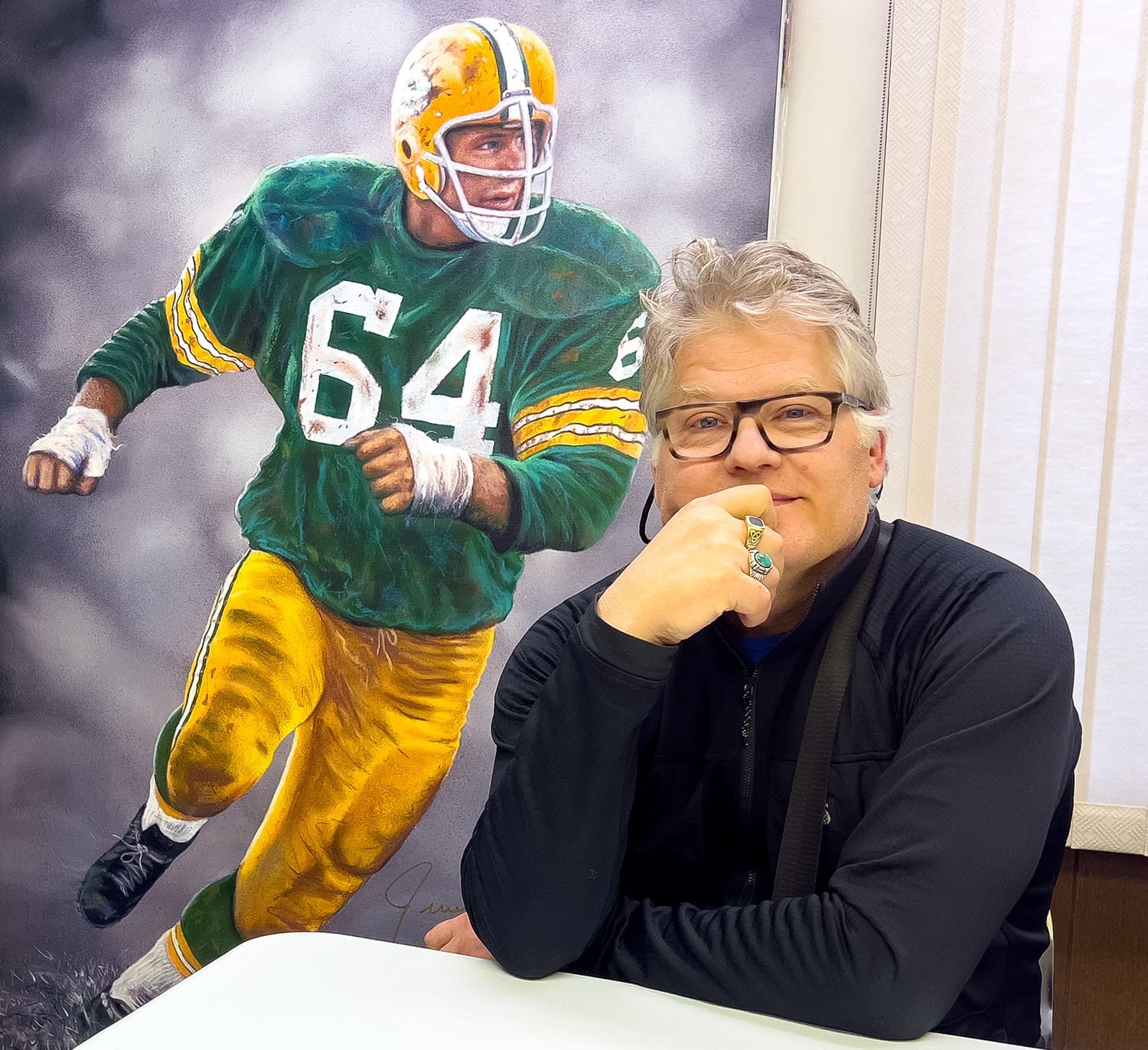Real estate agent sitting at a table, showcasing the interior design of a residential property, with artwork of a football player in a green and yellow uniform adding character to the space.