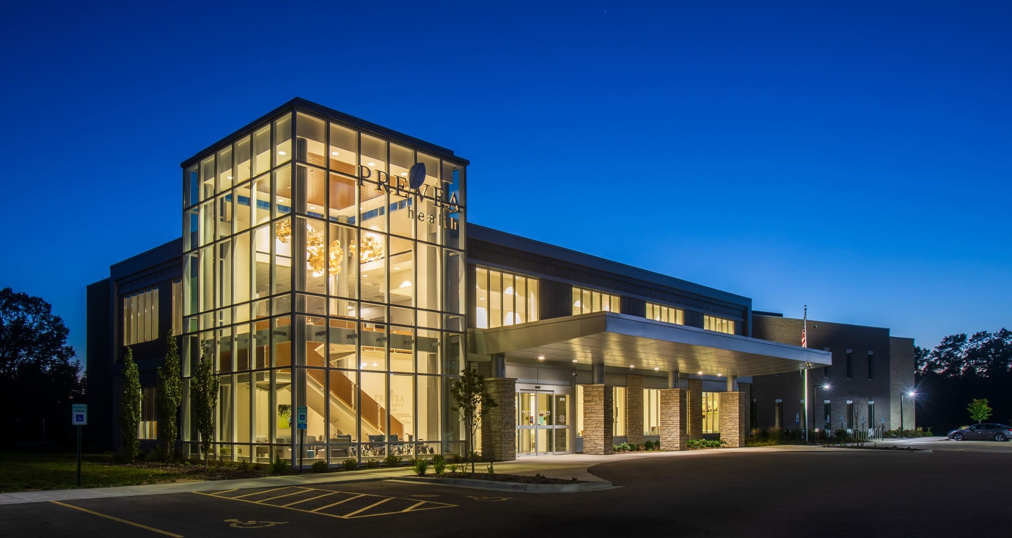 Contemporary commercial property with large glass windows, well-lit parking, and covered entry, photographed at dusk for real estate listing. Contemporary commercial property with large glass windows, well-lit parking, and covered entry, photographed at dusk for real estate listing.