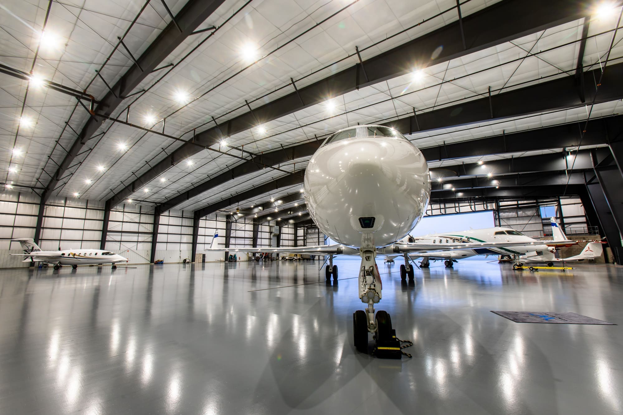 Spacious, modern commercial aircraft hangar with polished floors, high ceilings, and multiple private jets for luxury property listing. Spacious, modern commercial aircraft hangar with polished floors, high ceilings, and multiple private jets for luxury property listing.