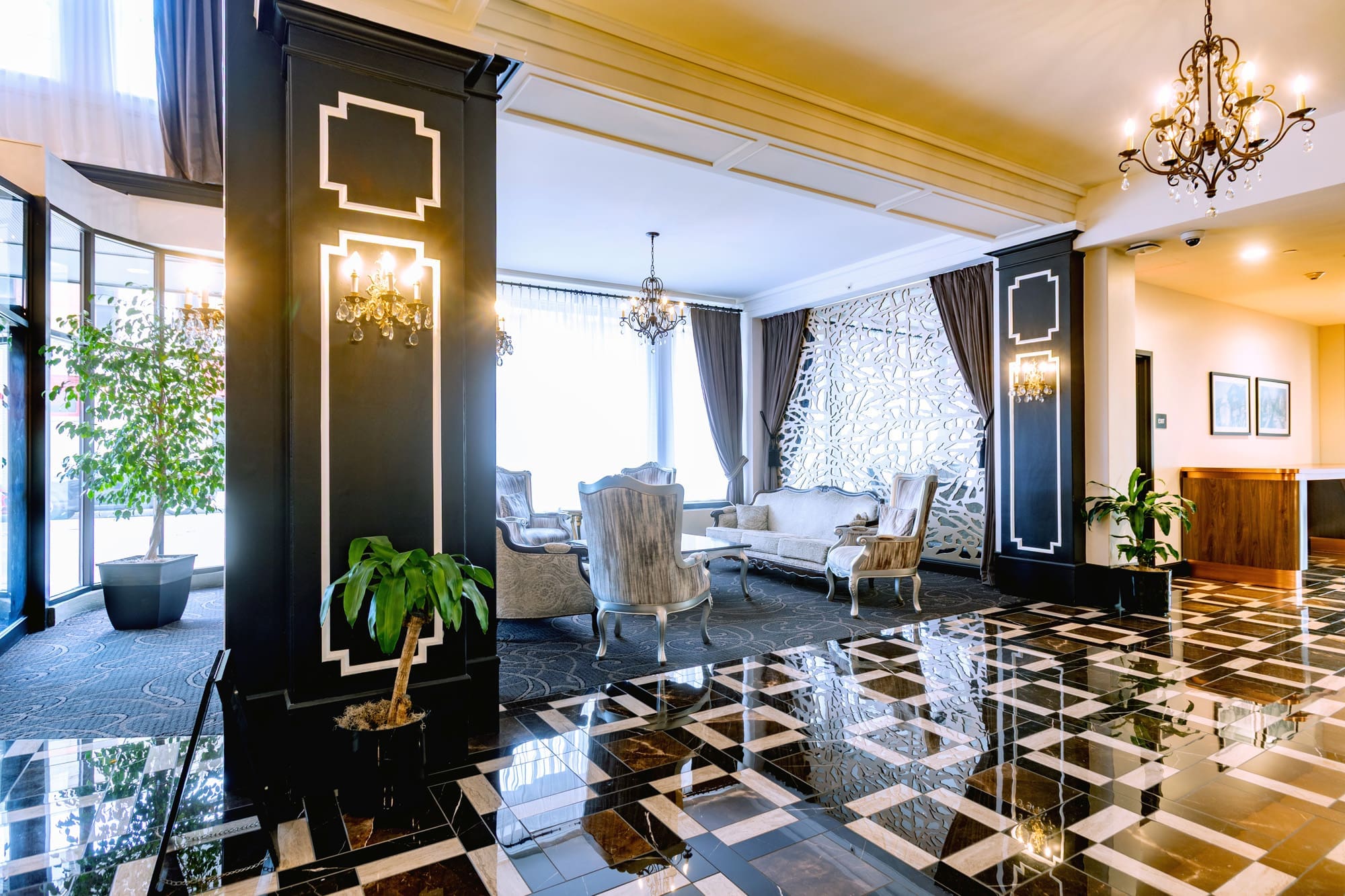 Spacious commercial hotel lobby featuring polished marble floors, black pillars, chandeliers, large windows, and modern decor.