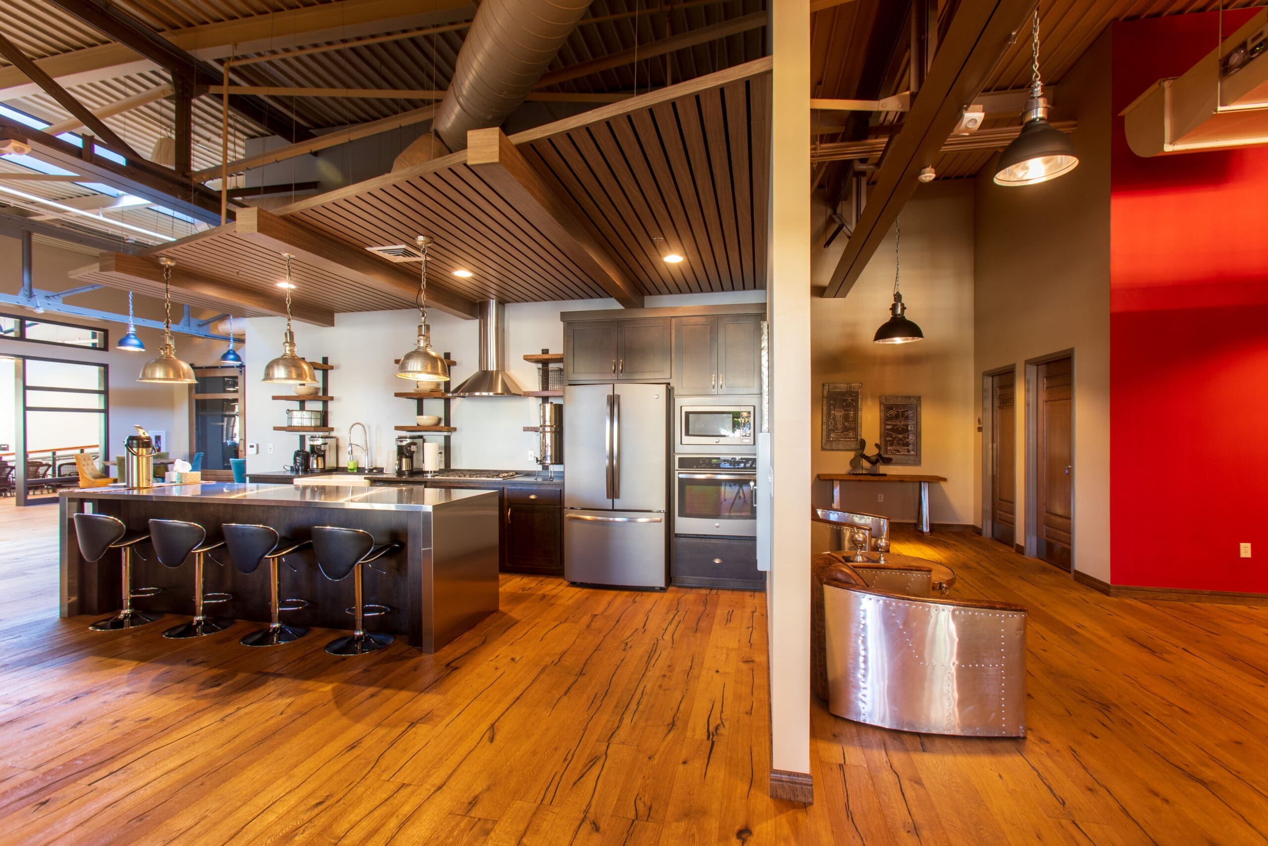 Contemporary industrial kitchen in a residential property with stainless steel appliances, wood floors, black bar stools, and red accent wall.