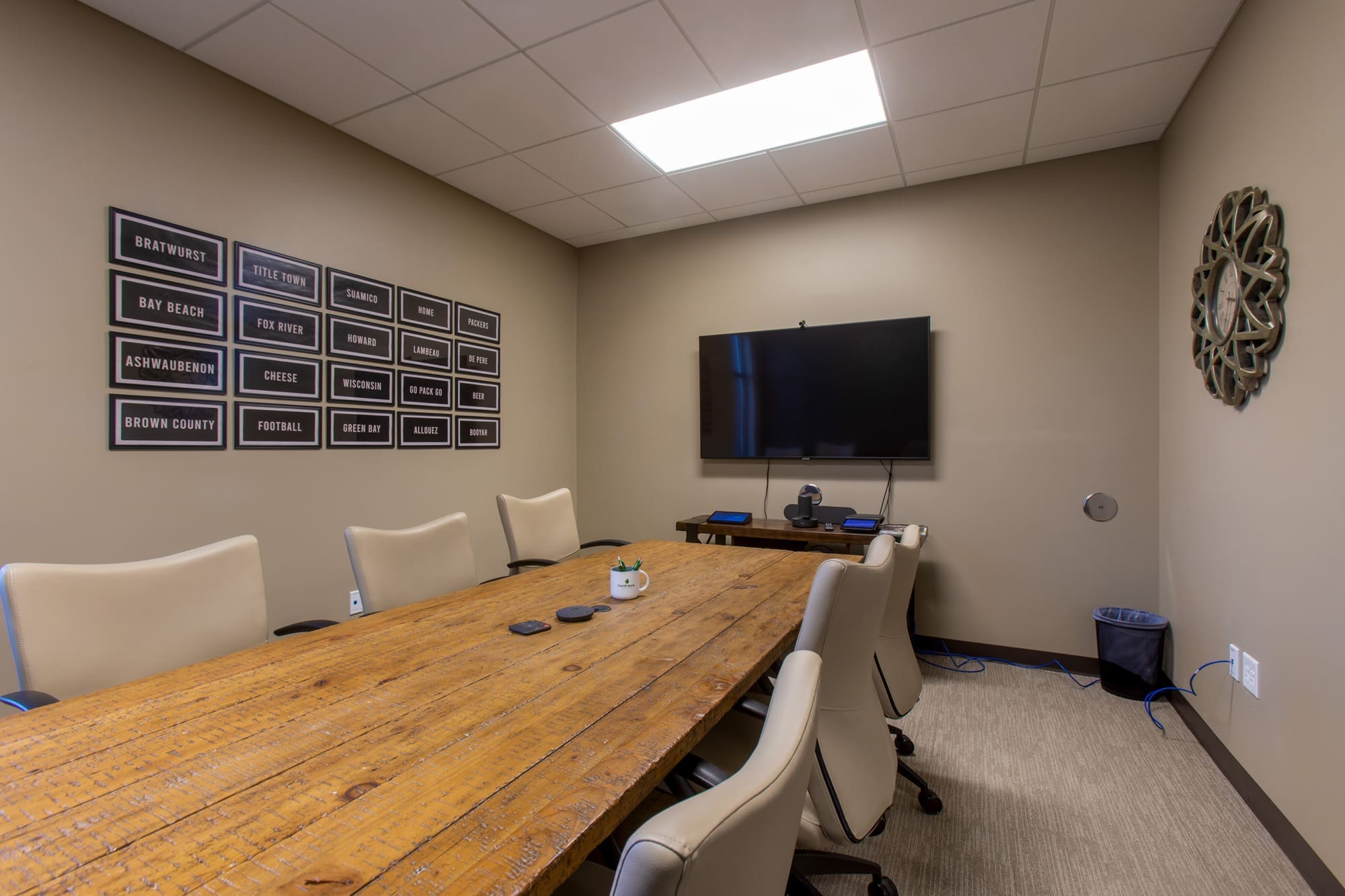 Modern commercial conference room features a wooden table, eight white chairs, wall-mounted TV, and stylish décor—ideal office space.