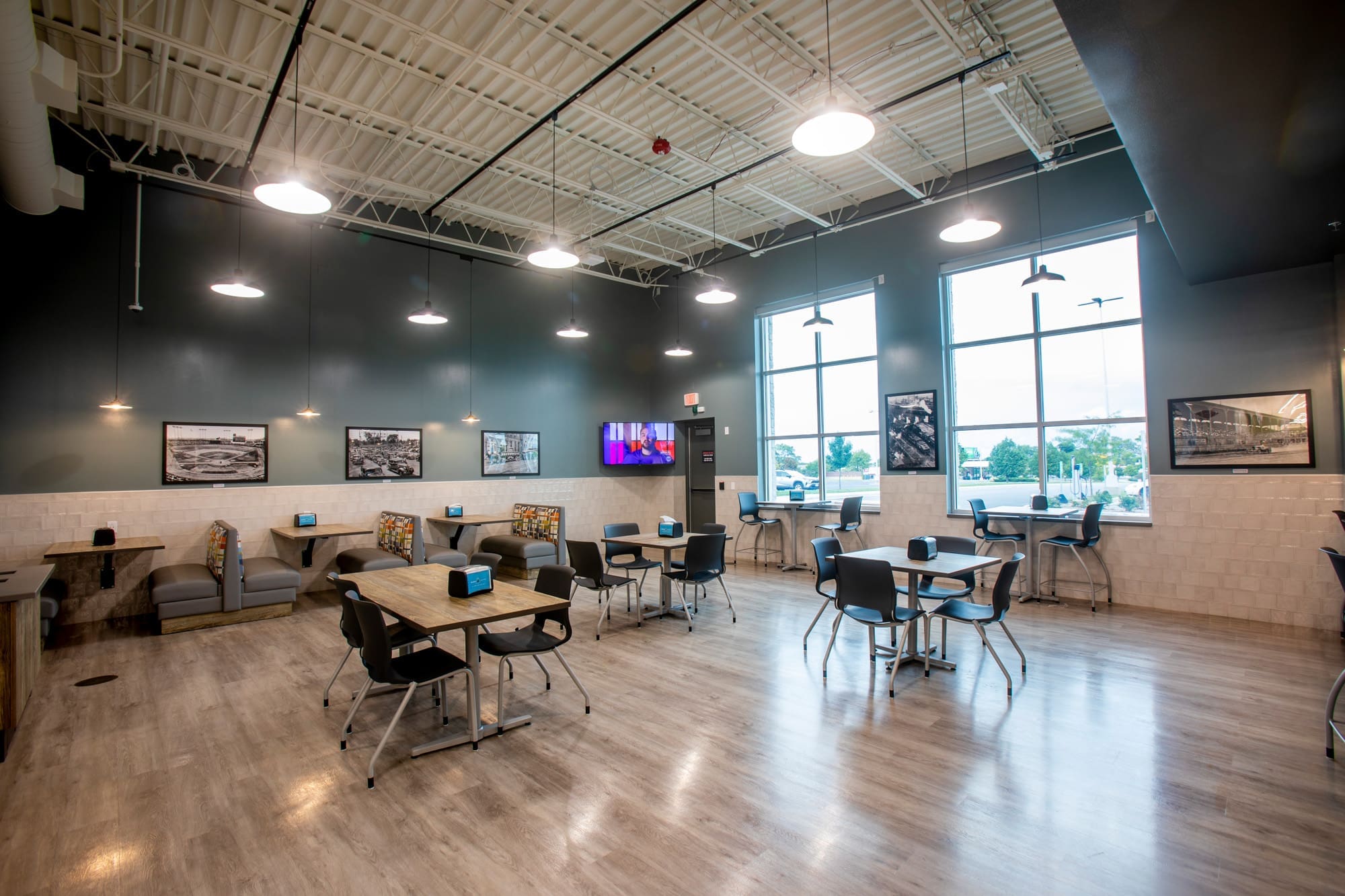 Commercial property break room with tables, booths, large windows, natural light, wall-mounted TV, and contemporary decor.